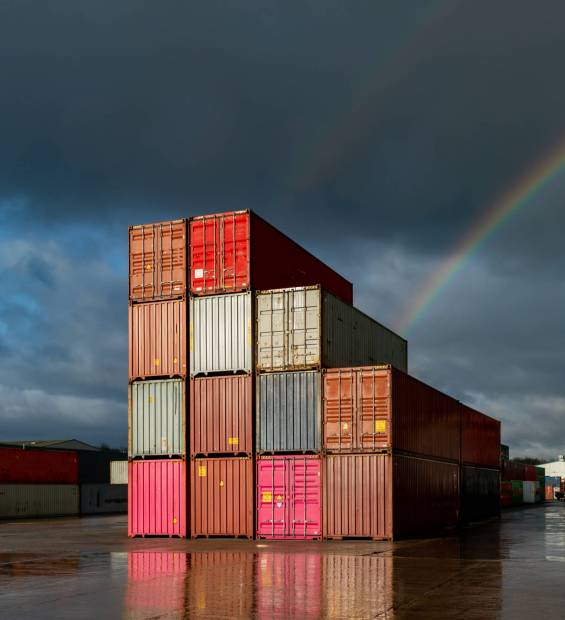 A stack of shipping containers on a deserted commercial dock with sunlight and rainbow